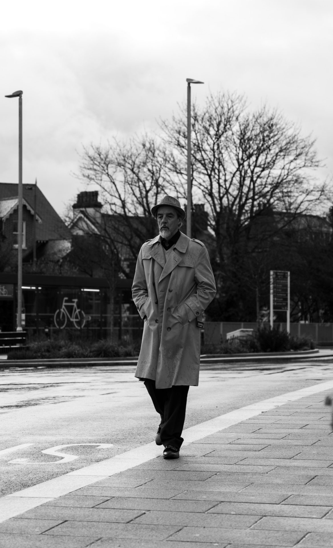 Man in trench coat and hat walking down a wet street