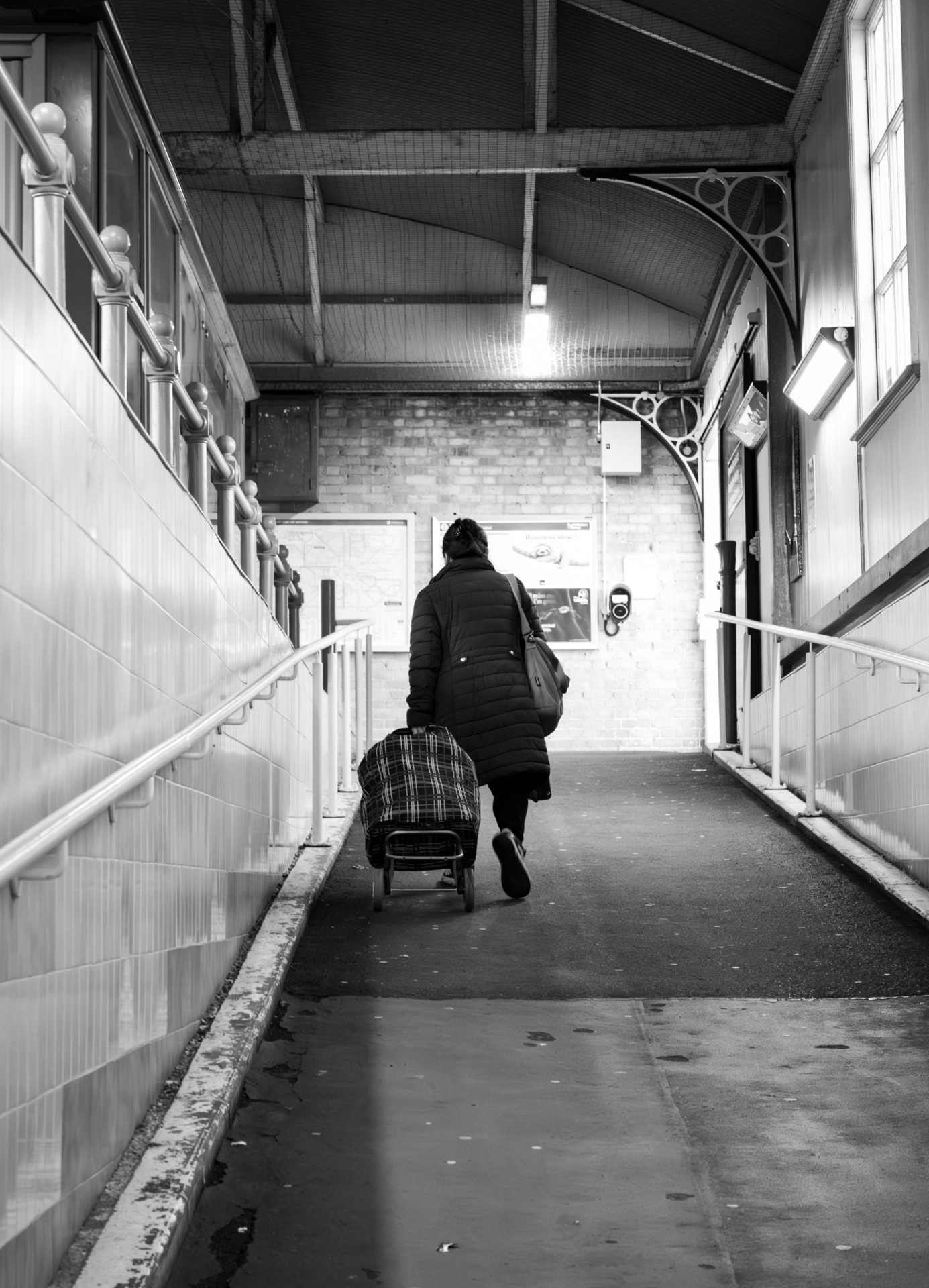Woman walking down a tiled station ramp with a shopping cart
