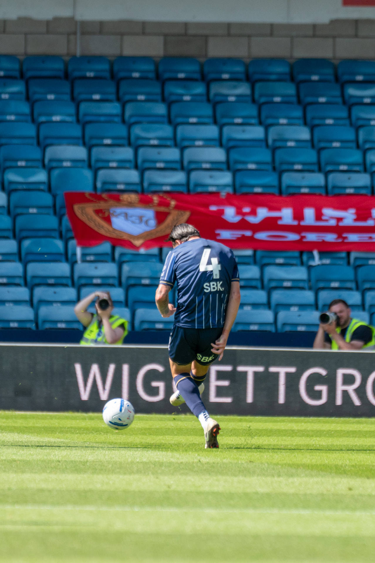 Player passing the ball with photographers behind the hoardings