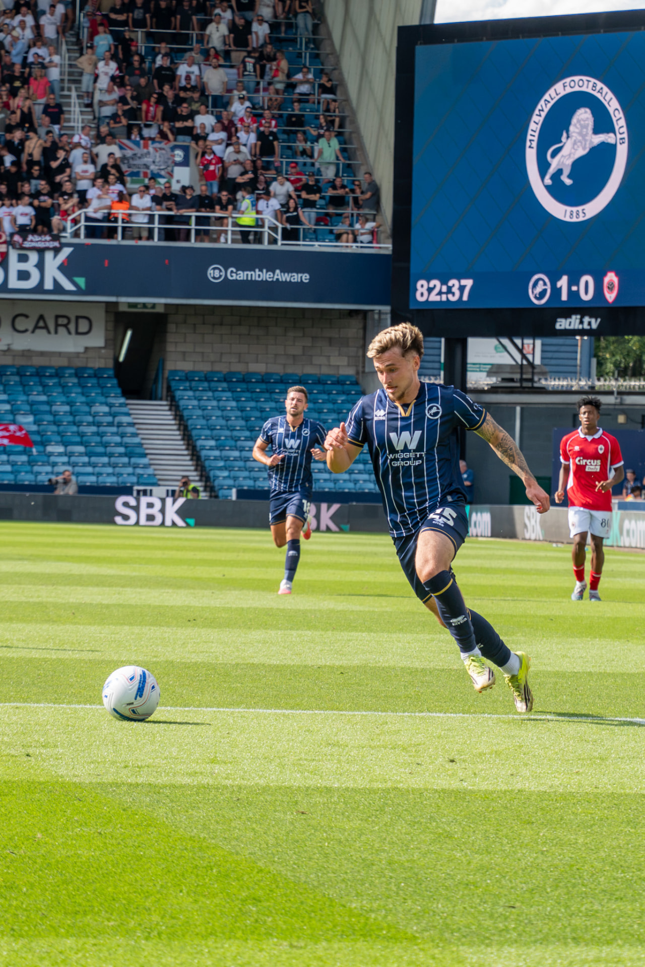 Millwall player driving at the defence with the scoreboard behind