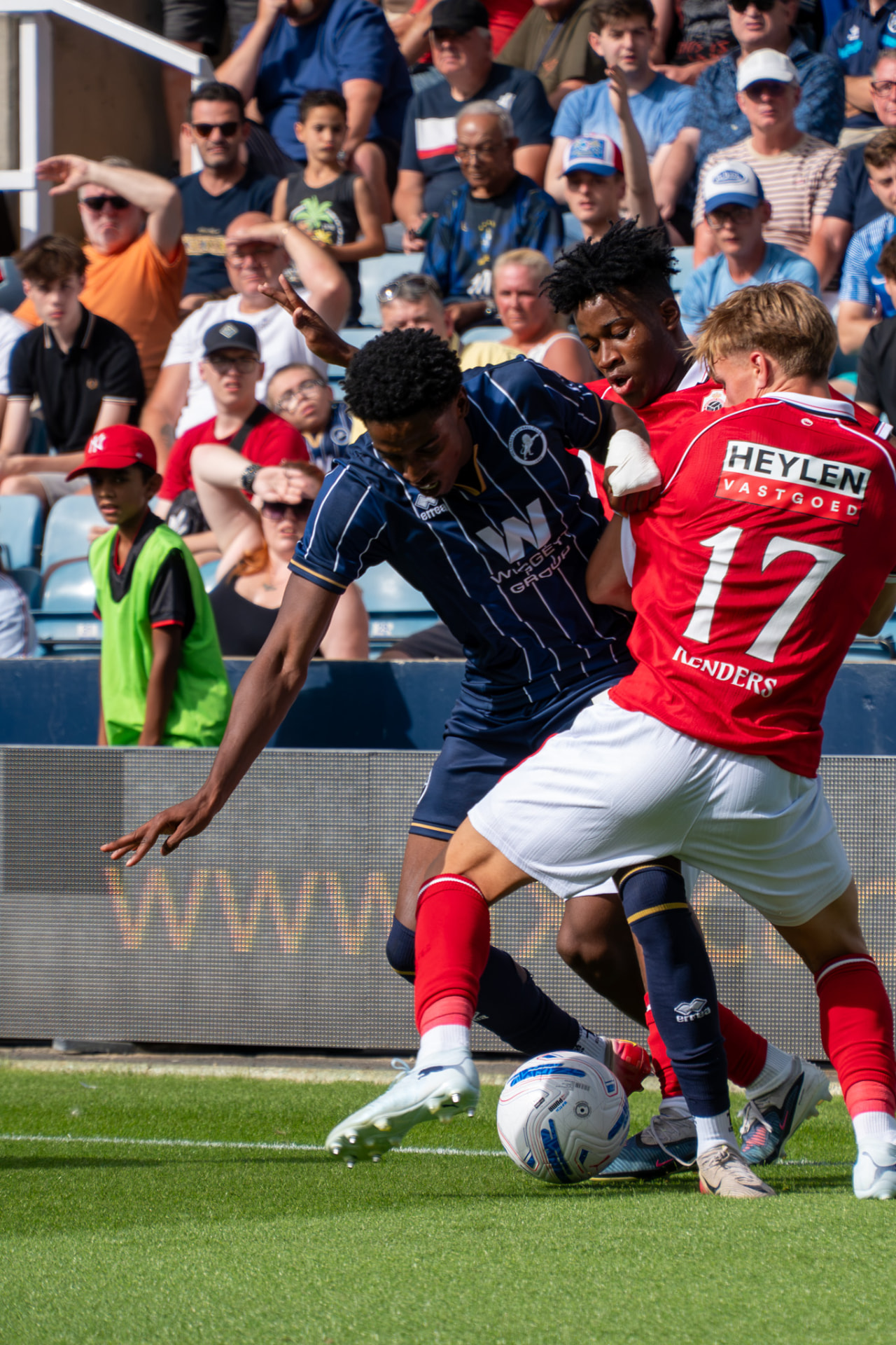 Millwall winger shielding the ball from two red-shirted opponents