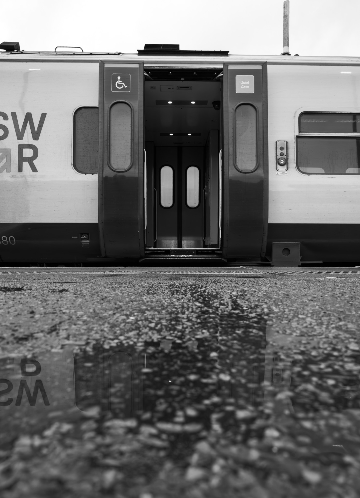 Open train doors reflected in a puddle on the platform